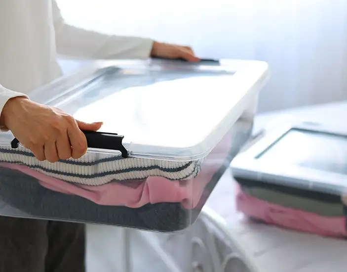 Photo of person holding a clear plastic tub of clothing